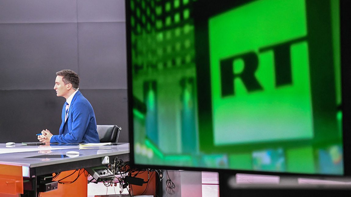 Un giornalista presenta la notizia in TV.  Sullo schermo dietro di lui c'è l'emblema di Russia Today.