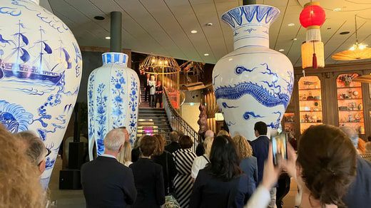 È in corso la cerimonia di apertura dell'albergo con interventi dalla scalinata della hall.  Riproduzioni giganti di vasi cinesi fanno parte della creazione di un ambiente che ricorda l'India orientale.