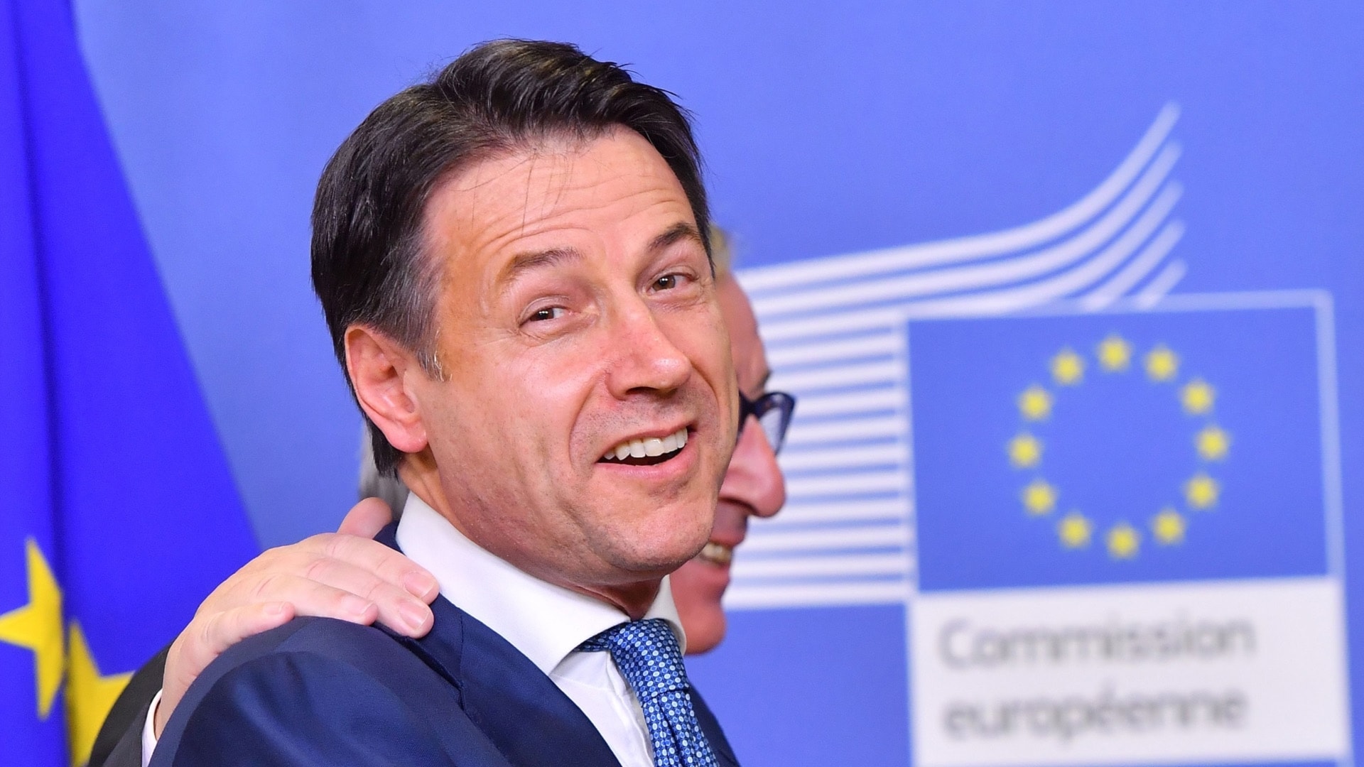 Jean-Claude Juncker och Giuseppe Conte håller om varandra och ser glada ut.